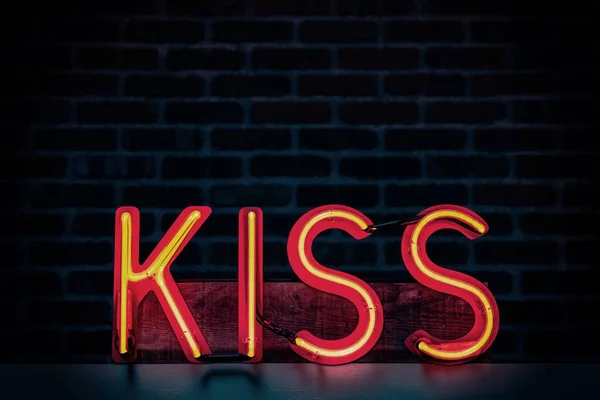 Zbliżenie zdjęcia podniecającego Pocałunek neon-light signage z tłem brązowej cegły ściany — Zdjęcie stockowe