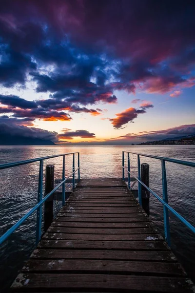 Belo tiro de uma doca de madeira perto do mar com o reflexo do pôr do sol sob o céu nublado — Fotografia de Stock