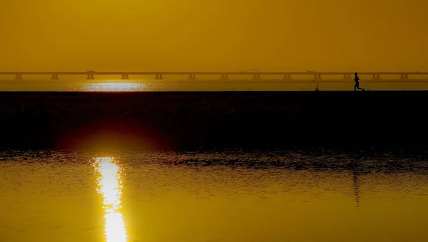 一张美丽的照片 是一个人带着日落的倒影在海面上的码头上奔跑 — 图库照片