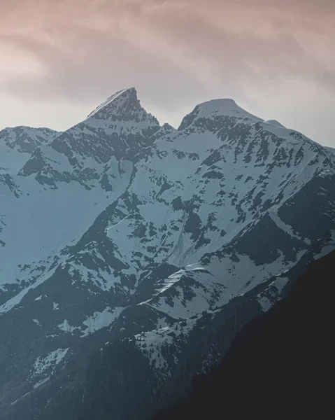 Pionowe Ujęcie Pięknych Pokrytych Śniegiem Szczytów Górskich Pod Chmurnym Niebem — Zdjęcie stockowe
