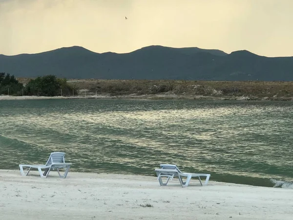 高い岩の山々に囲まれた狂気の海の波の近くに2つの折りたたみ椅子を持つ美しいビーチ — ストック写真