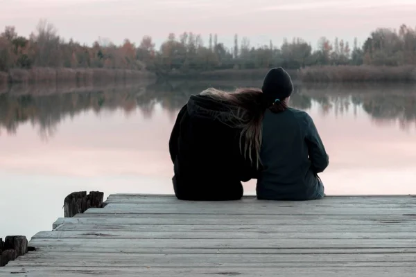 Amis assis sur un quai en bois avec l'un d'eux reposant sa tête sur l'épaule près de la mer — Photo