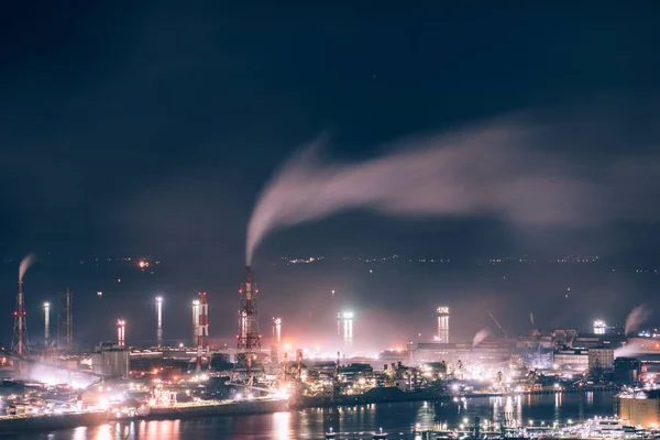 Photo d'une usine et de fumée entourée de lumières et d'eau sous un ciel nocturne — Photo