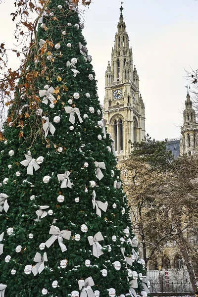 Plan vertical d'un sapin de Noël décoré avec un bâtiment historique en béton en arrière-plan — Photo