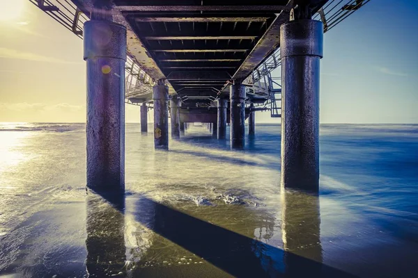 Pontile di cemento vicino al mare ondulato con il riflesso del sole luminoso — Foto Stock