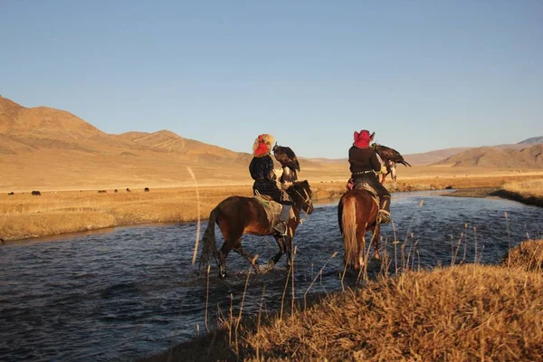 Foto di due cavalieri in un fiume circondato da una valle deserta con colline sullo sfondo — Foto Stock