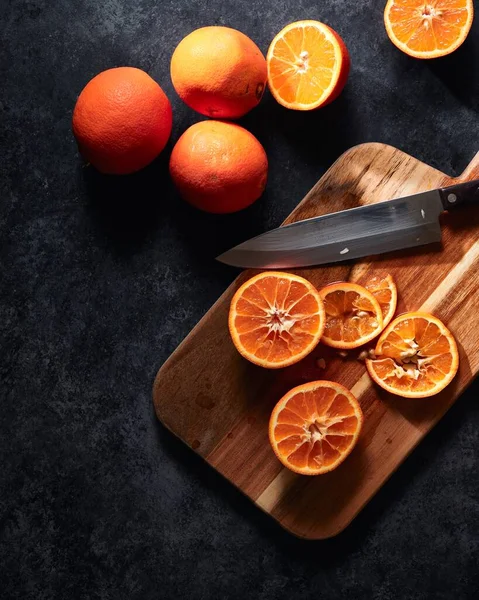 Függőleges lövés szeletelt narancs és egy kést a vágódeszka fekete alapon — Stock Fotó