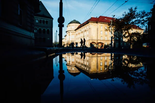 Puddle con el reflejo de un edificio blanco y gente caminando por la calle — Foto de Stock