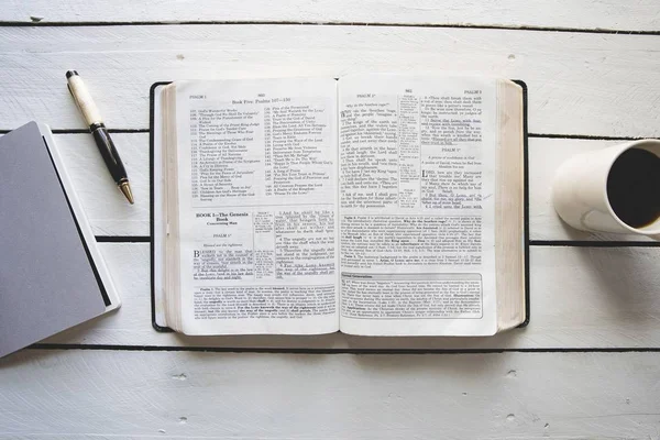 Vue aérienne d'une bible ouverte entre un café et un bloc-notes avec un stylo — Photo