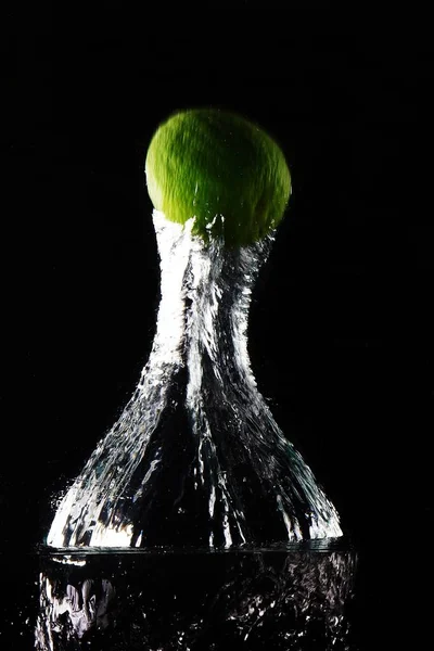 Verticaal schot van een groene vrucht in het water gegooid met een wazige achtergrond — Stockfoto