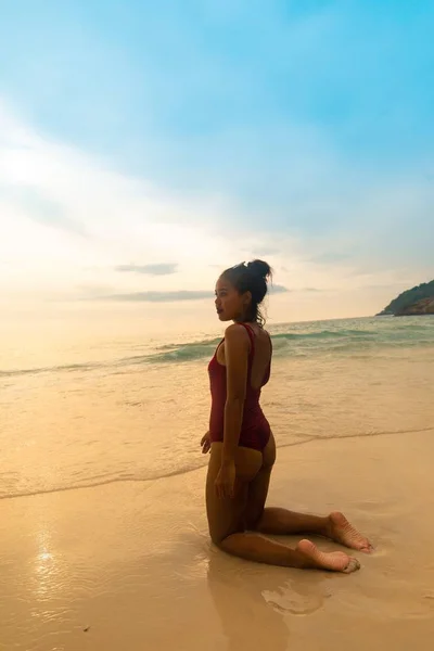 日の出の間砂浜に座っている赤い水着を着た女性の垂直ショット — ストック写真