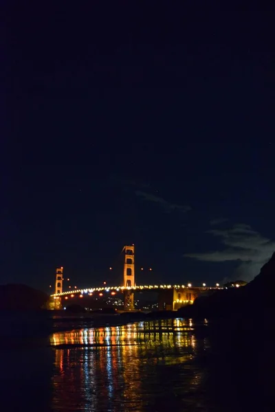 Golden Gate Bridge with the bridge lights on reflecting on the water during the night — ストック写真