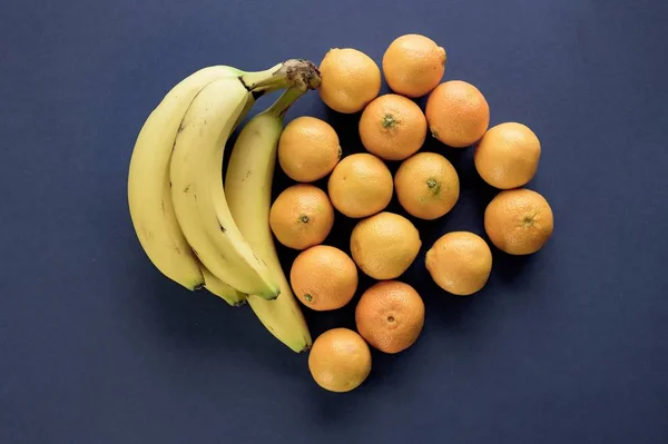 Tiro de close-up de laranjas e banana fazendo uma forma de coração em uma superfície azul escura — Fotografia de Stock