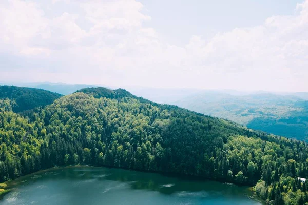 Vysoký úhel záběr na krásné jezero obklopené stromy pokryté horami pod zamračenou oblohou — Stock fotografie