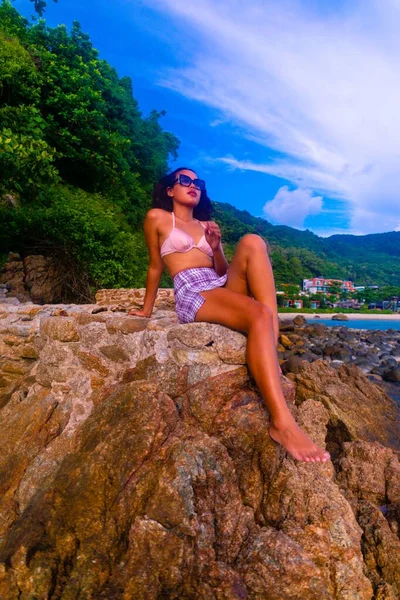 ビーチで素敵な一日を楽しむ岩の形成に座って魅力的な女性の垂直ショット — ストック写真