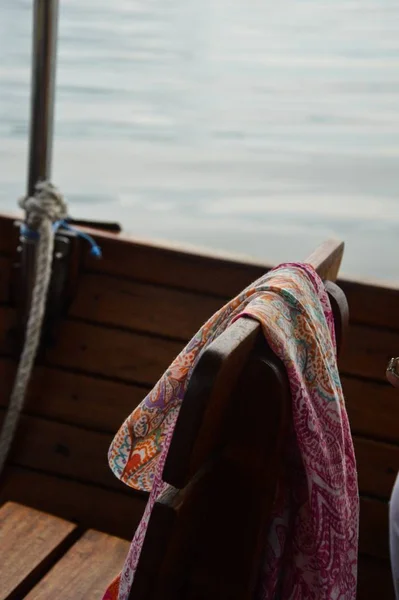 Κοντινό πλάνο ενός πολύχρωμου σάλι σε μια ξύλινη καρέκλα σε μια βάρκα με τη θάλασσα στο θολό φόντο — Φωτογραφία Αρχείου