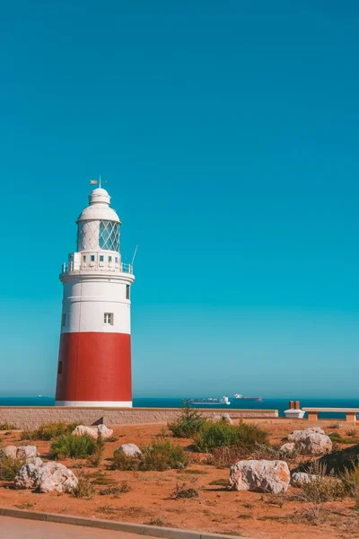 White and red lighthouse in a sea in The United Kingdom surrounded by stones and greenery — Stock Photo, Image
