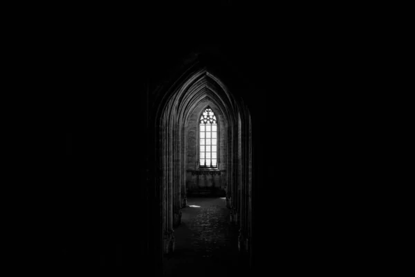 Серый снимок окна в конце арочного коридора в темном старом здании — стоковое фото