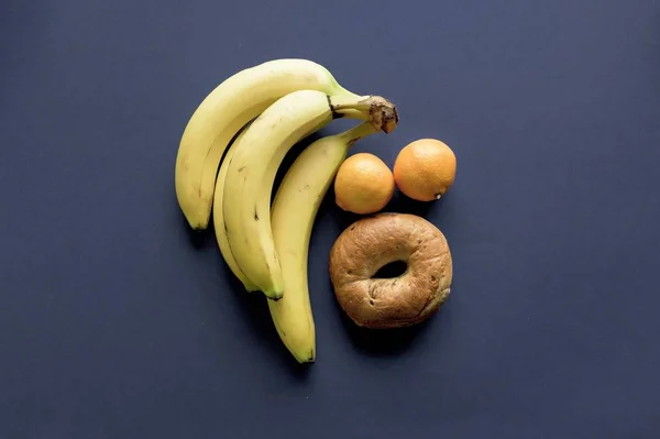 Donkerblauw oppervlak met sinaasappels, banaan en donut eroverheen — Stockfoto