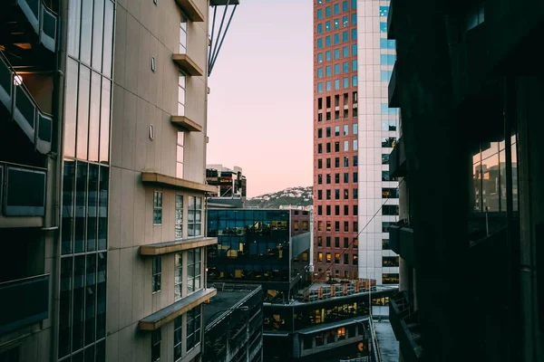 Bela vista de arranha-céus modernos coloridos com uma cidade no fundo durante o pôr do sol — Fotografia de Stock