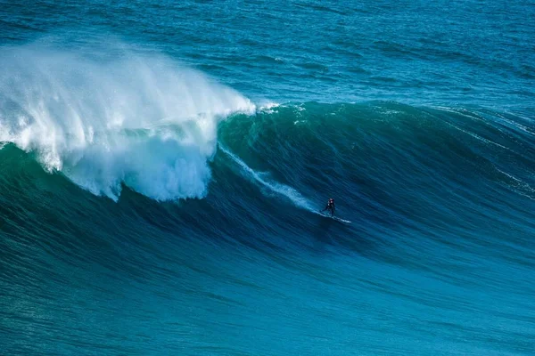 Surfer sailing through the foamy waves of the Atlantic Ocean towards the shore of Nazare, Portugal — стоковое фото