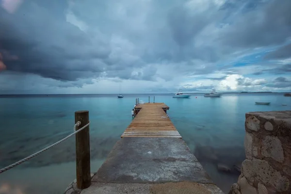 Belo tiro de um cais que leva ao oceano sob o céu sombrio em Bonaire, Caribe — Fotografia de Stock