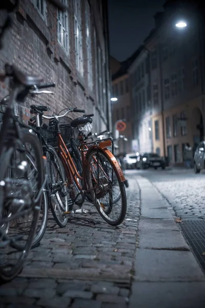 Vertical shot of bicycles parked on the sidewalk in the street at night — Stock Photo, Image