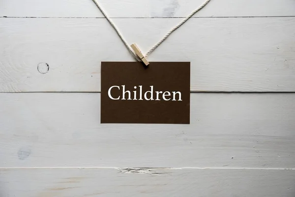 Nahaufnahme eines Schildes an einem Seil mit darauf geschriebenen Kindern und weißem Holzhintergrund — Stockfoto