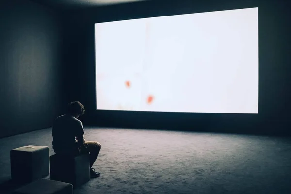 Personne assise dans une pièce sombre devant un écran de projection — Photo