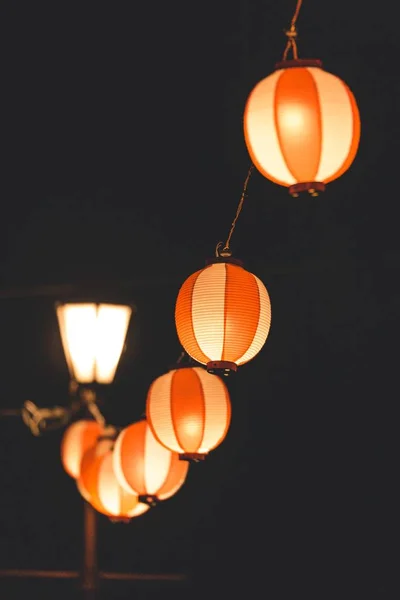 Vertikal bild av orange papperslyktor hängande från en tråd som sprider ljus under natten — Stockfoto