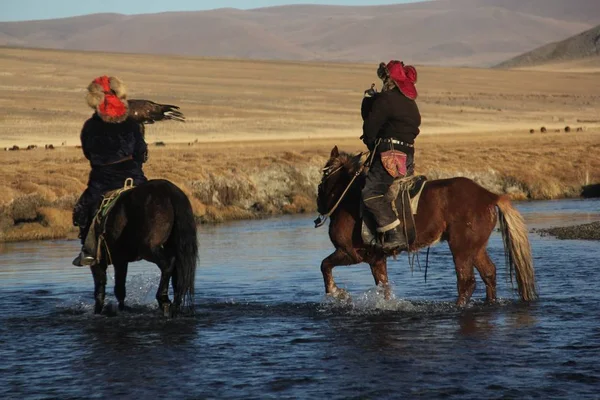 Foto di due cavalieri in un fiume circondato da una valle deserta sotto un cielo blu — Foto Stock