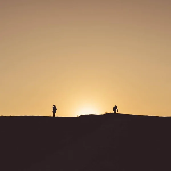 Kleine Silhouetten von Menschen, die auf dem Land gehen, mit dem gelben Sonnenuntergang im Hintergrund — Stockfoto