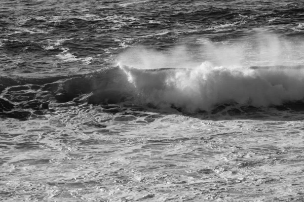 Fechar imagem em escala de cinza das ondas do oceano salpicando em direção à costa durante um pôr do sol quente — Fotografia de Stock