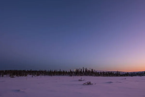 Gün batımında arka planda ağaçlar ve dağlar olan karla kaplı bir tarlanın manzarası — Stok fotoğraf