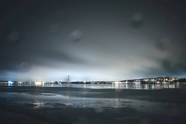 Bela paisagem noturna de luzes da cidade refletindo no mar sob o céu sombrio — Fotografia de Stock