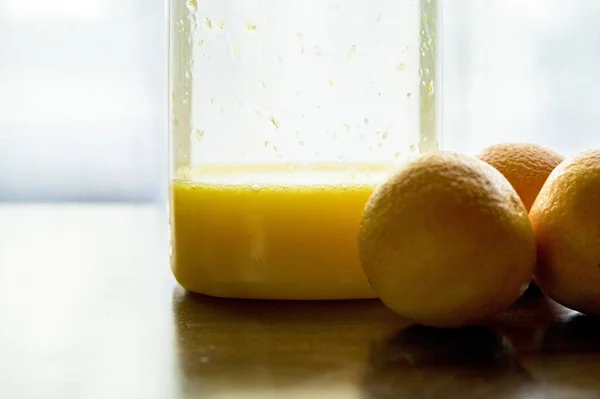Κοντινό πλάνο πορτοκάλια κοντά σε ένα βάζο γεμάτο χυμό πορτοκαλιού — Φωτογραφία Αρχείου