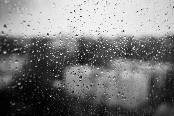 Снимок в сером цвете стекла, покрытого капельками дождя на размытом фоне — стоковое фото