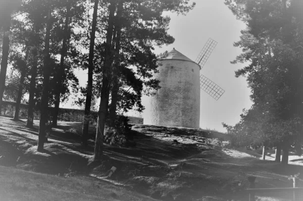 Kasvetli gökyüzünün altındaki tepede bir yel değirmeninin gri ölçekli görüntüsü. — Stok fotoğraf