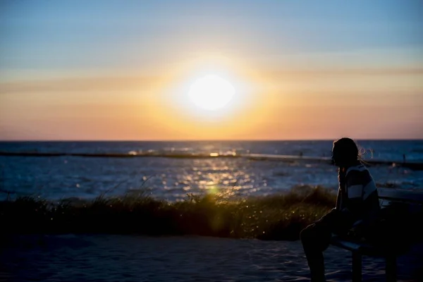 Female sitting on the bench near the sea at sunset — Stock Photo, Image