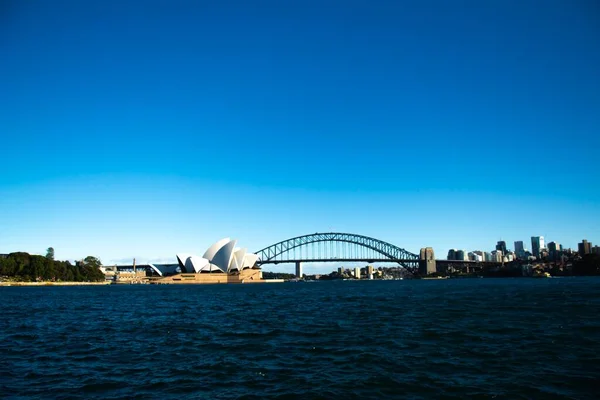 Paesaggio di un mare sotto un cielo blu con un ponte e una città sullo sfondo — Foto Stock