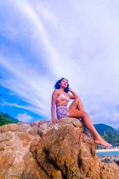 ビーチで素敵な一日を楽しむ岩の形成に座って魅力的な女性の垂直ショット — ストック写真