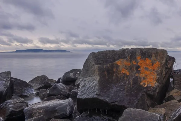 Oranje verf op een grote steen bij de oceaan onder de donkere bewolkte lucht — Stockfoto