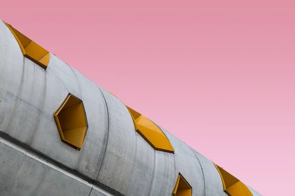 Baixo ângulo tiro de estrutura de concreto com molduras de janela amarelas em um fundo rosa — Fotografia de Stock