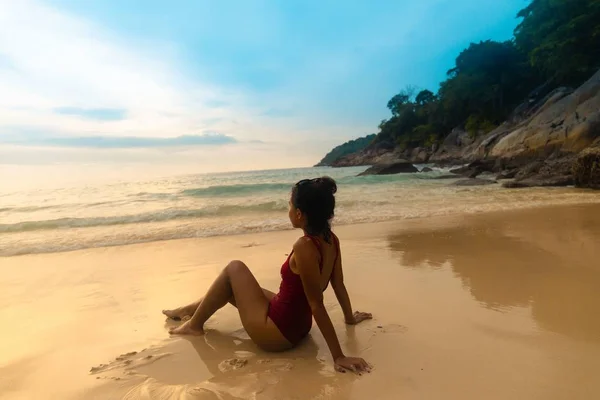 日の出の間砂浜に座っている赤い水着を着た魅力的な女性 — ストック写真