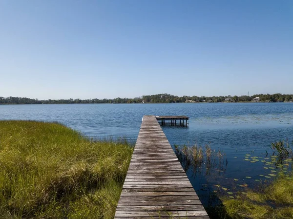 背後に青い空のある芝生の海岸近くの水の上の木道 — ストック写真
