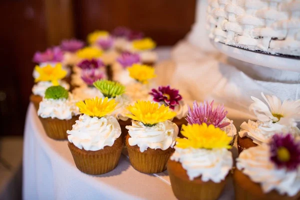 背景がぼやけている白いテーブルの上に異なる花を持つカップケーキの多く — ストック写真