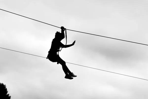 Greyscale tiro de uma pessoa em uma corrida de tirolesa sob o céu limpo — Fotografia de Stock