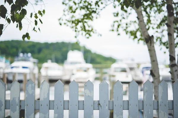 Schöne Aufnahme von weißem Zaun mit verschwommenen Booten und Bäumen im Hintergrund — Stockfoto