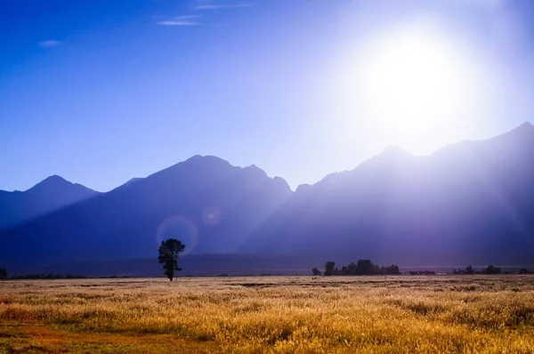 Impresionante toma del sol saliendo sobre un campo rodeado de un paisaje montañoso — Foto de Stock