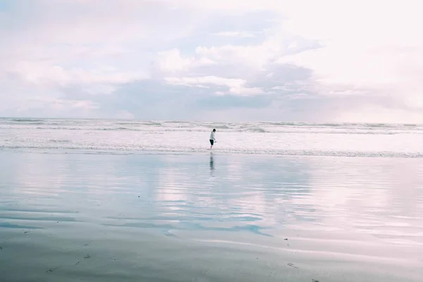 Jovem fêmea caminhando ao longo da costa perto das ondas marinhas loucas durante o dia — Fotografia de Stock